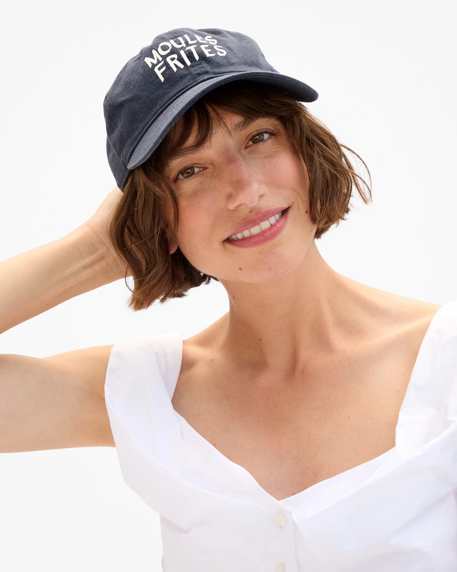 Woman wearing a navy blue cap with 'Moules Frites' text on a white background