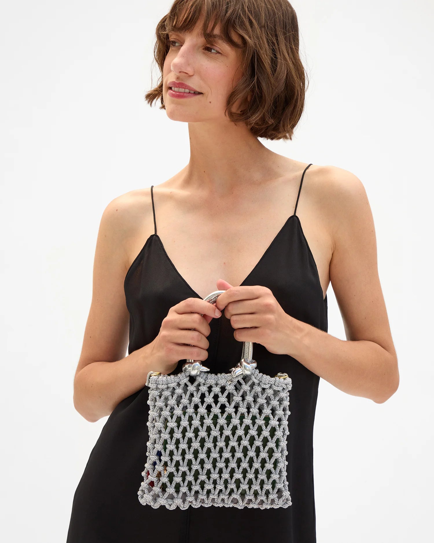 Woman holding a white beaded handbag against a plain background