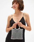 Woman holding a white beaded handbag against a plain background
