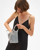 Woman holding a white woven handbag against a plain background