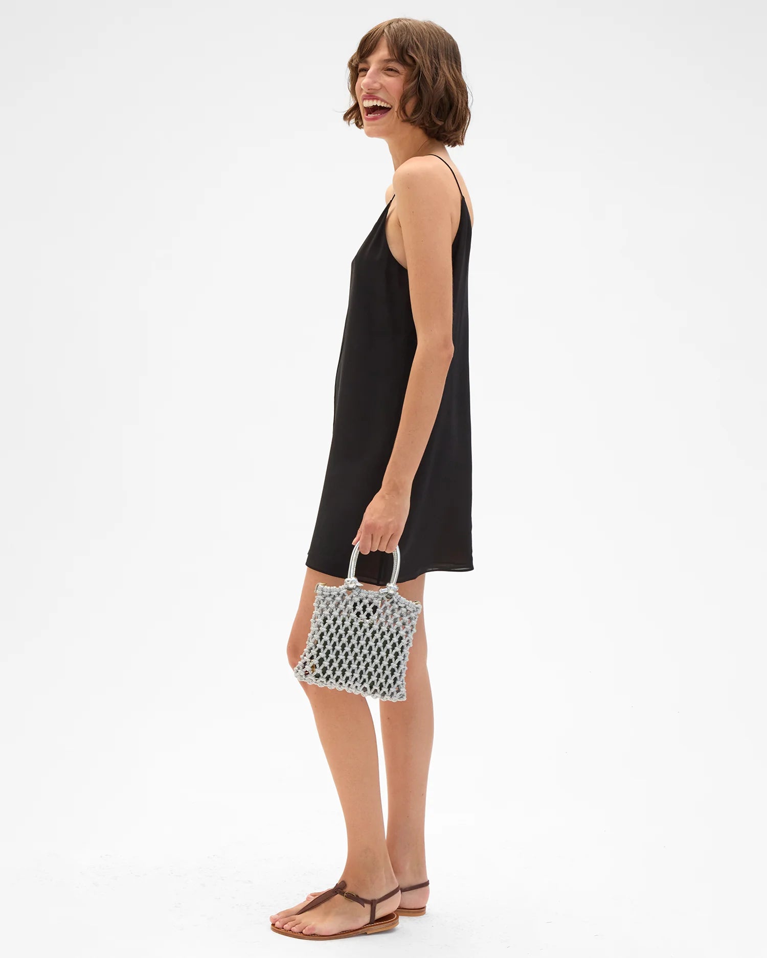 Woman in a black dress holding a patterned handbag on a white background