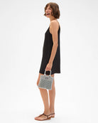 Woman in a black dress holding a patterned handbag on a white background