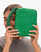 Person holding a green woven handbag in front of their face on a white background