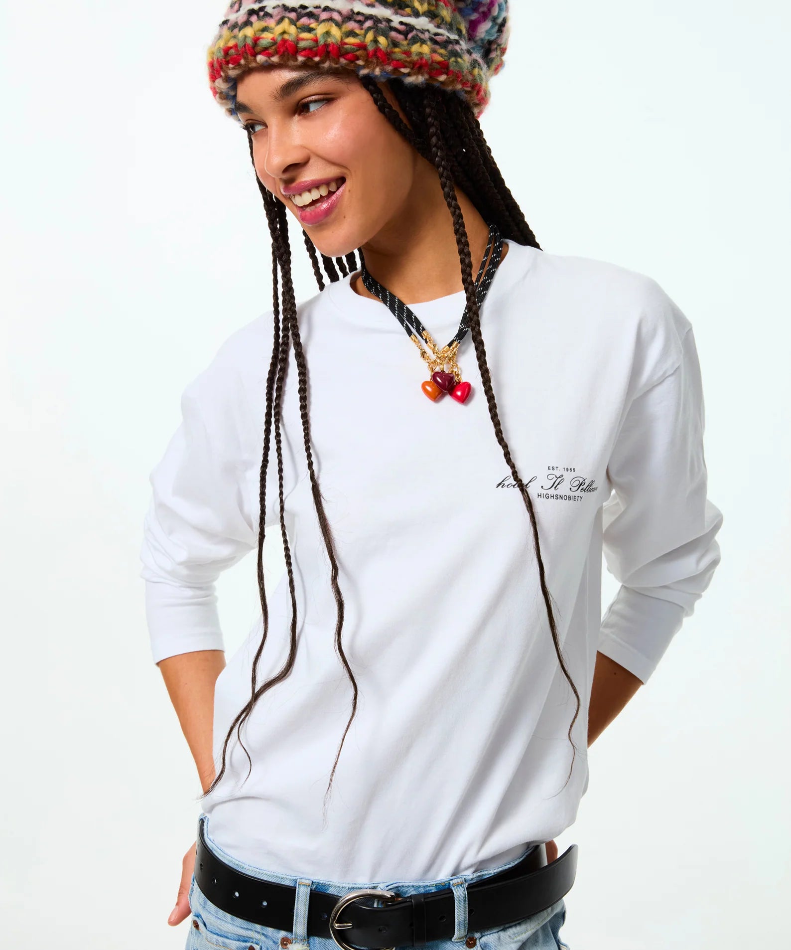 Person wearing a white long-sleeve shirt with text, colorful knit hat, and braided hair on a white background