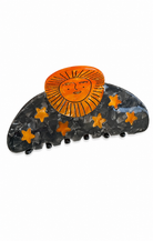A semi-circular hair claw clip featuring a glossy dark gray marbled base decorated with orange stars, topped with a bright orange sun face design.