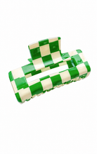 A glossy hair claw clip featuring a green and cream checkered pattern, shown on a plain white background.