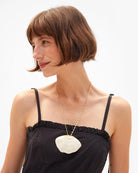 Woman wearing a black dress with a white floral pendant necklace on a white background