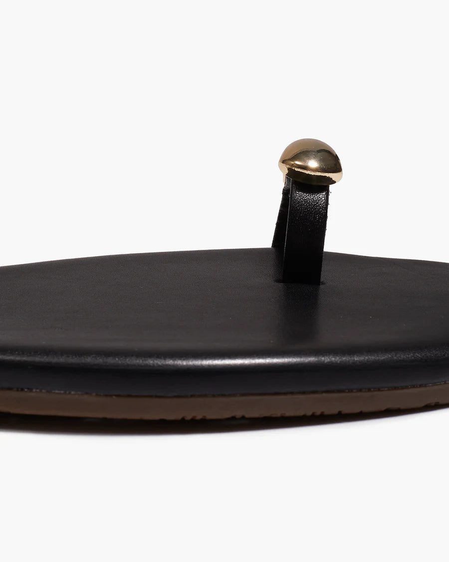 Black sandal with a gold toe ring on a white background