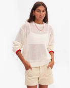 Woman wearing a white knit sweater with red trim and beige shorts on a white background