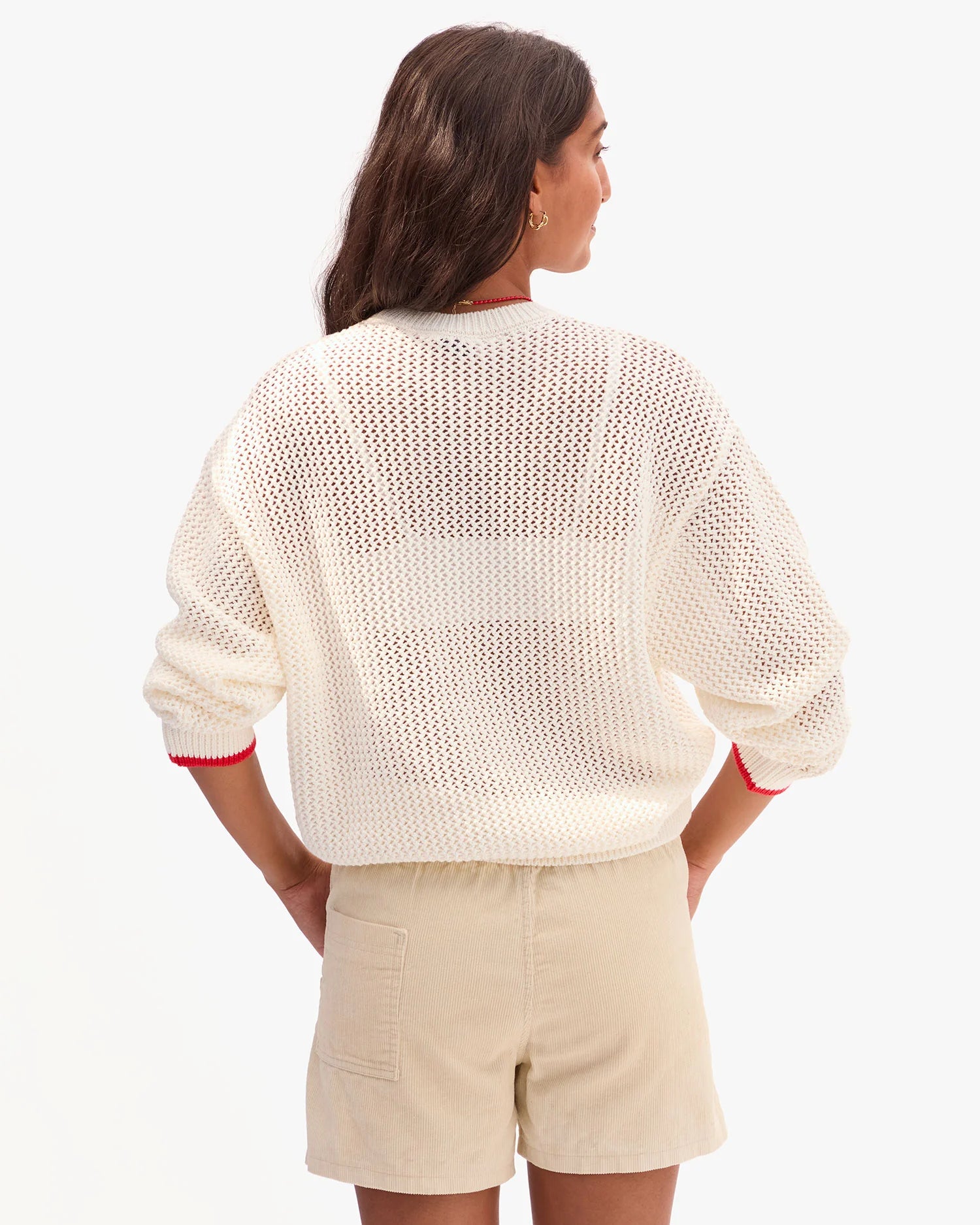 Woman wearing a cream knitted cardigan and beige shorts on a white background