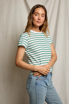 Woman wearing a green and white striped shirt and blue jeans against a plain background