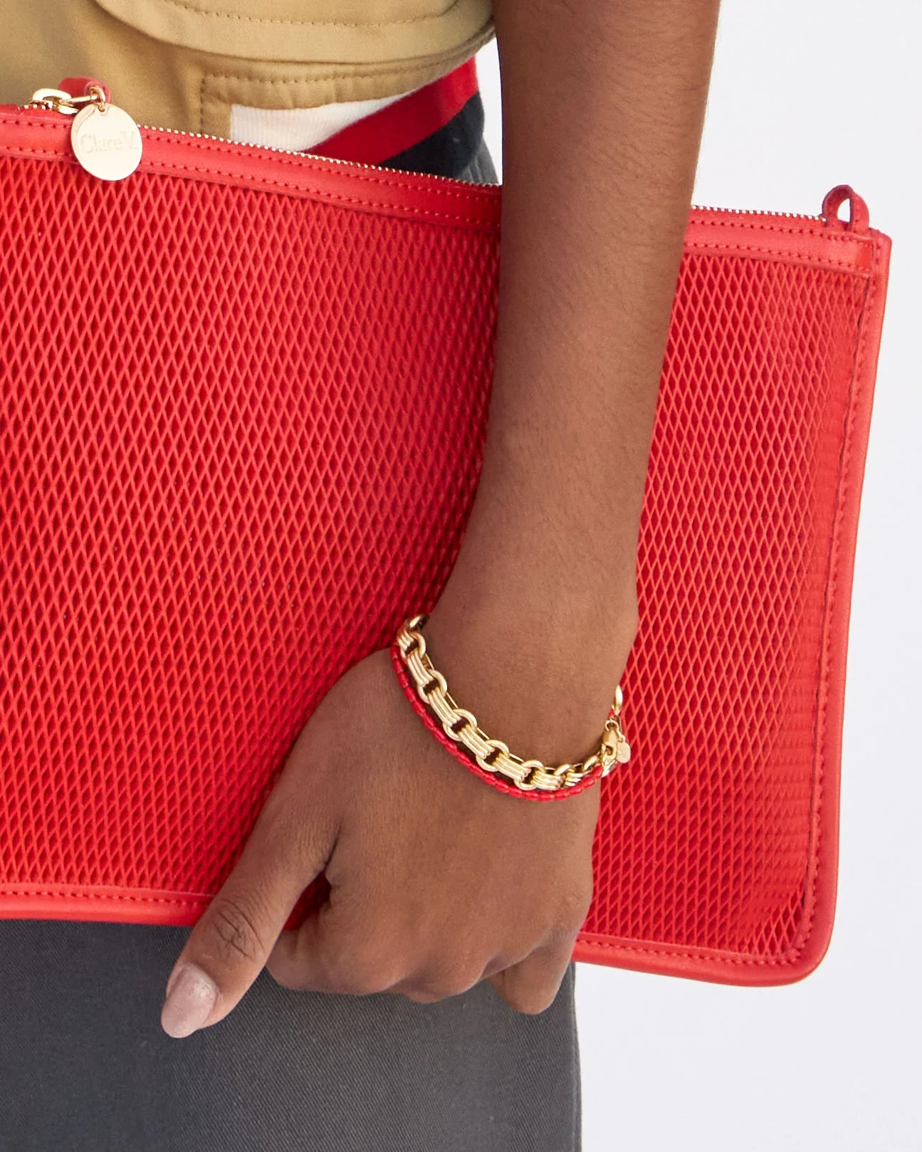 Red mesh clutch held by a hand with a gold bracelet on a light gray background