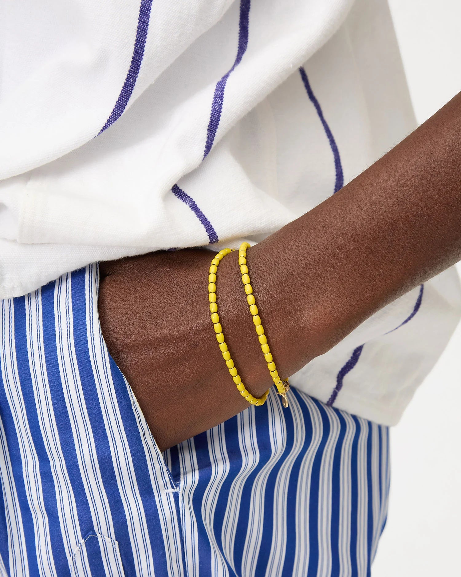 Yellow beaded bracelet on a wrist with a white and blue striped shirt