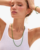 Woman wearing a white tank top and green beaded necklace with a blurred background
