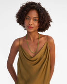 Woman wearing a mustard yellow dress with a green necklace on a plain background
