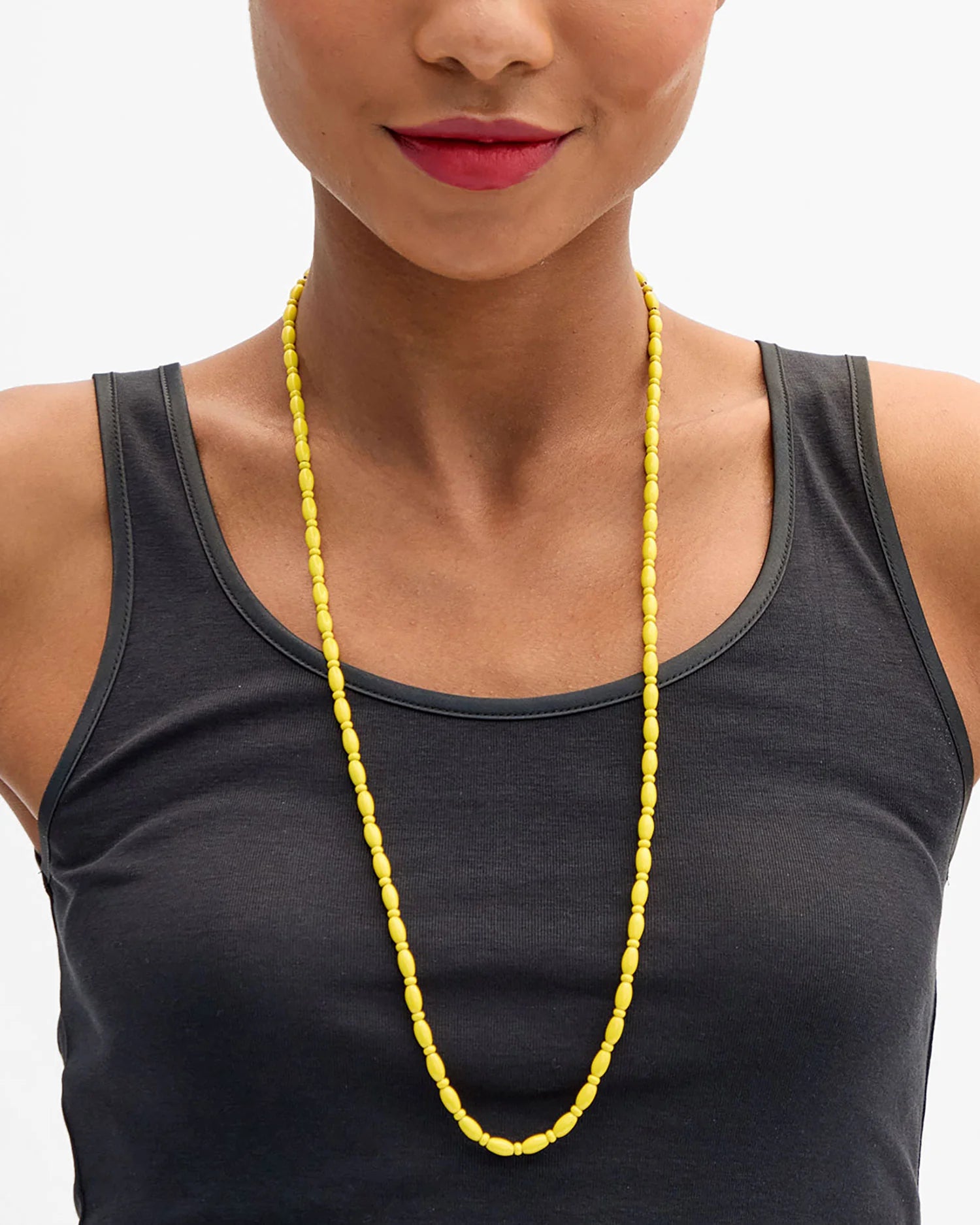 Woman wearing a black tank top and yellow necklace on a gray background