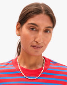 Woman wearing a red and blue striped shirt with a gold necklace and earrings on a white background