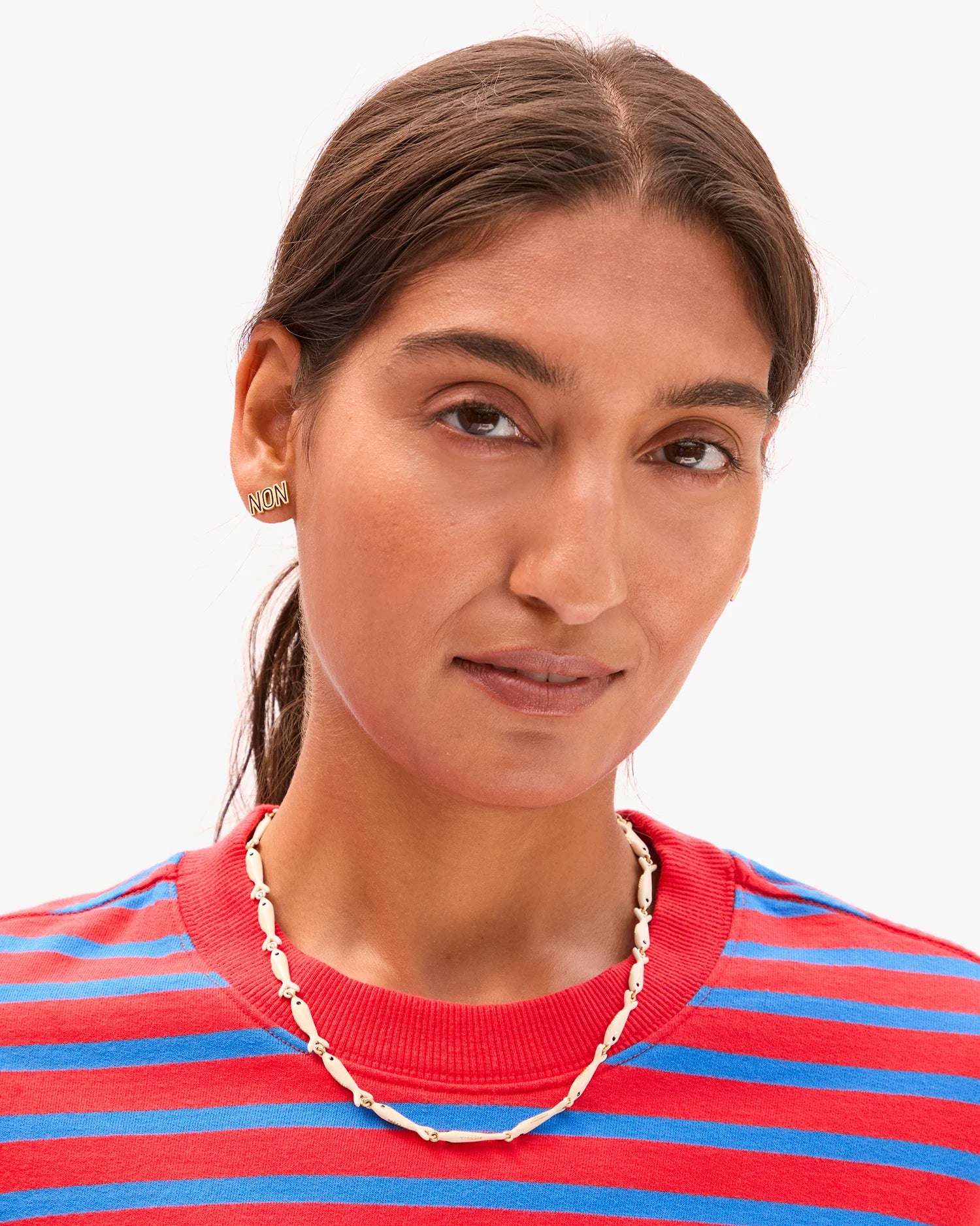 Woman wearing a red and blue striped shirt with a gold necklace and earrings on a white background