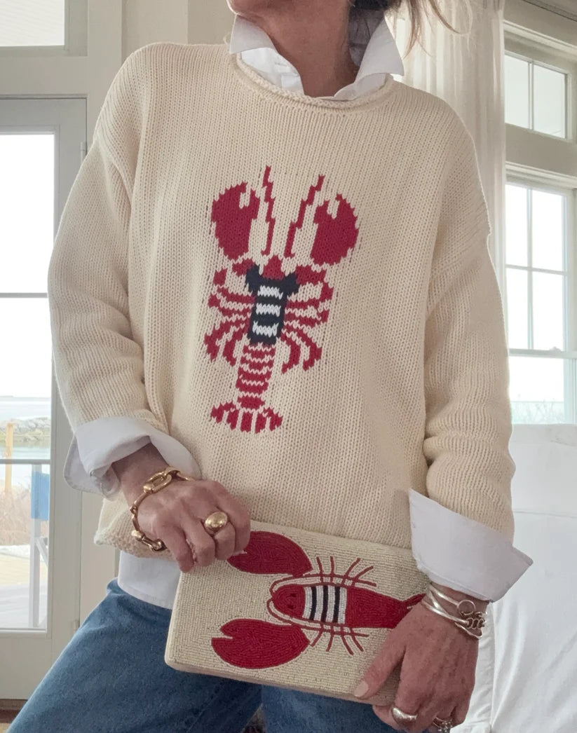 Person wearing a cream sweater with a red lobster design, holding a matching pouch.