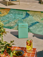 Teal Fieldbar cooler by a poolside with a glass of fruit salad.