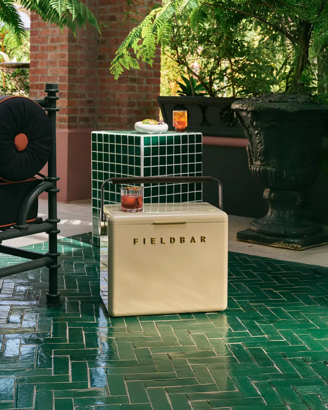 Beige Fieldbar cooler on a green tiled patio with a small table and drinks in the background.
