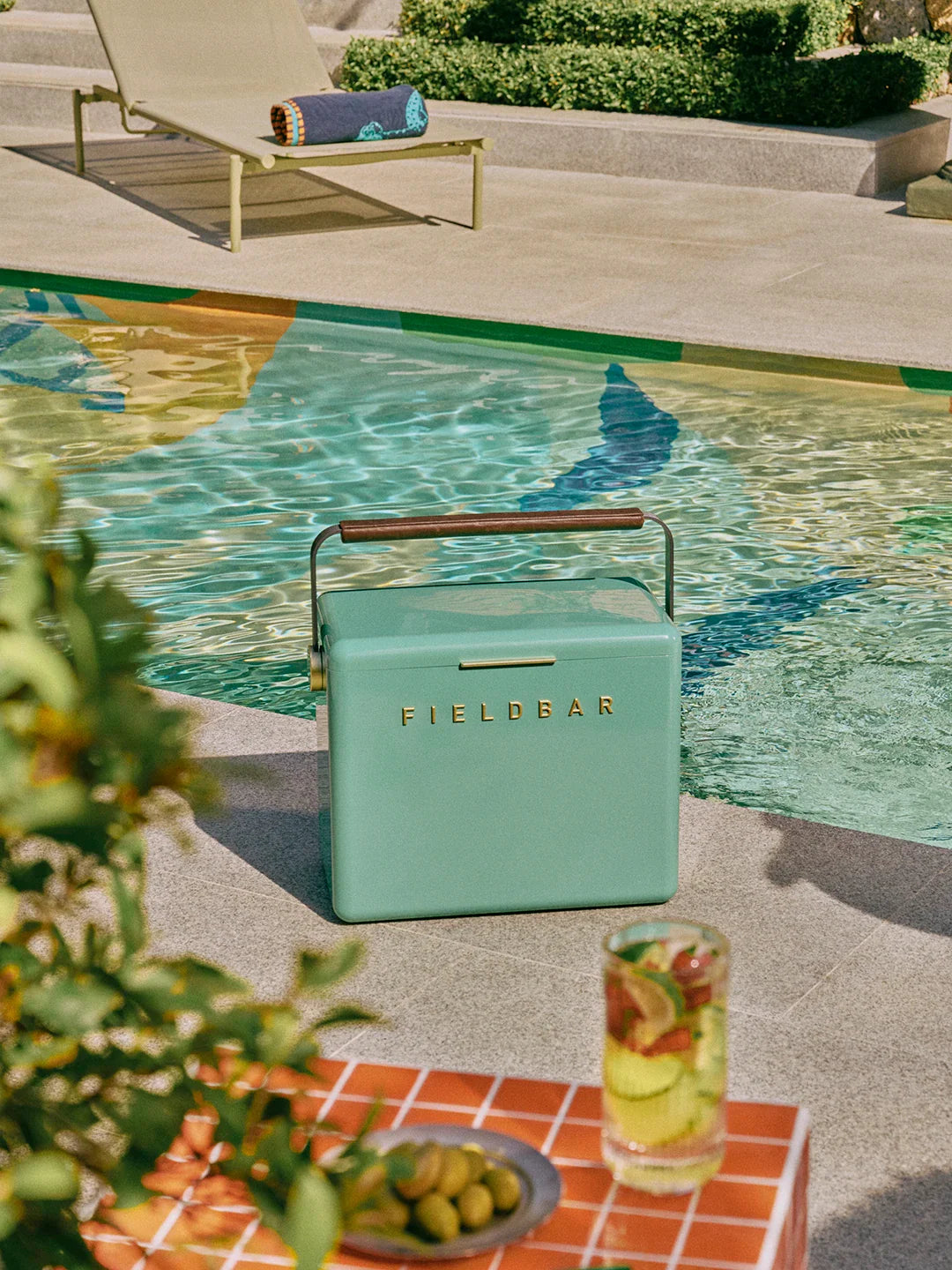 Teal Fieldbar cooler by a poolside with a glass of lemonade and snacks.