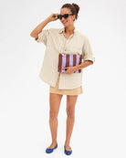 Woman holding a striped clutch and wearing sunglasses on a white background