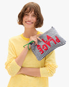Woman holding a striped pouch with 'PLAGE' text, wearing a yellow striped shirt.