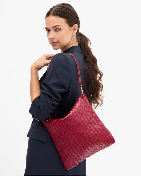 A woman wearing a navy blazer and skirt carries a woven red shoulder bag with gold hardware against a plain white background.