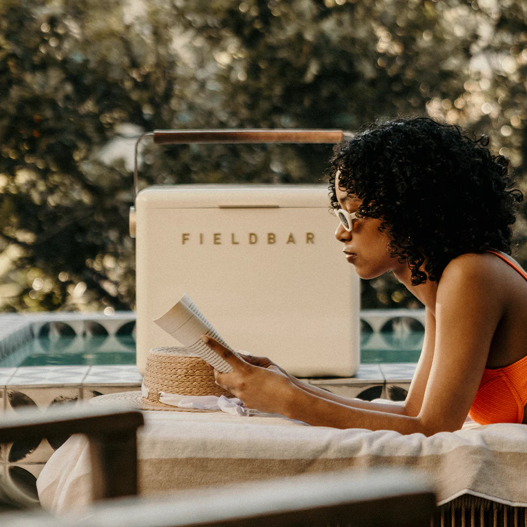 Woman reading a book by a pool with a Fieldbar cooler in the background