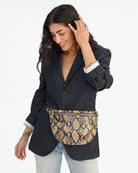 Woman wearing a dark denim jacket and snake print belt bag on a white background
