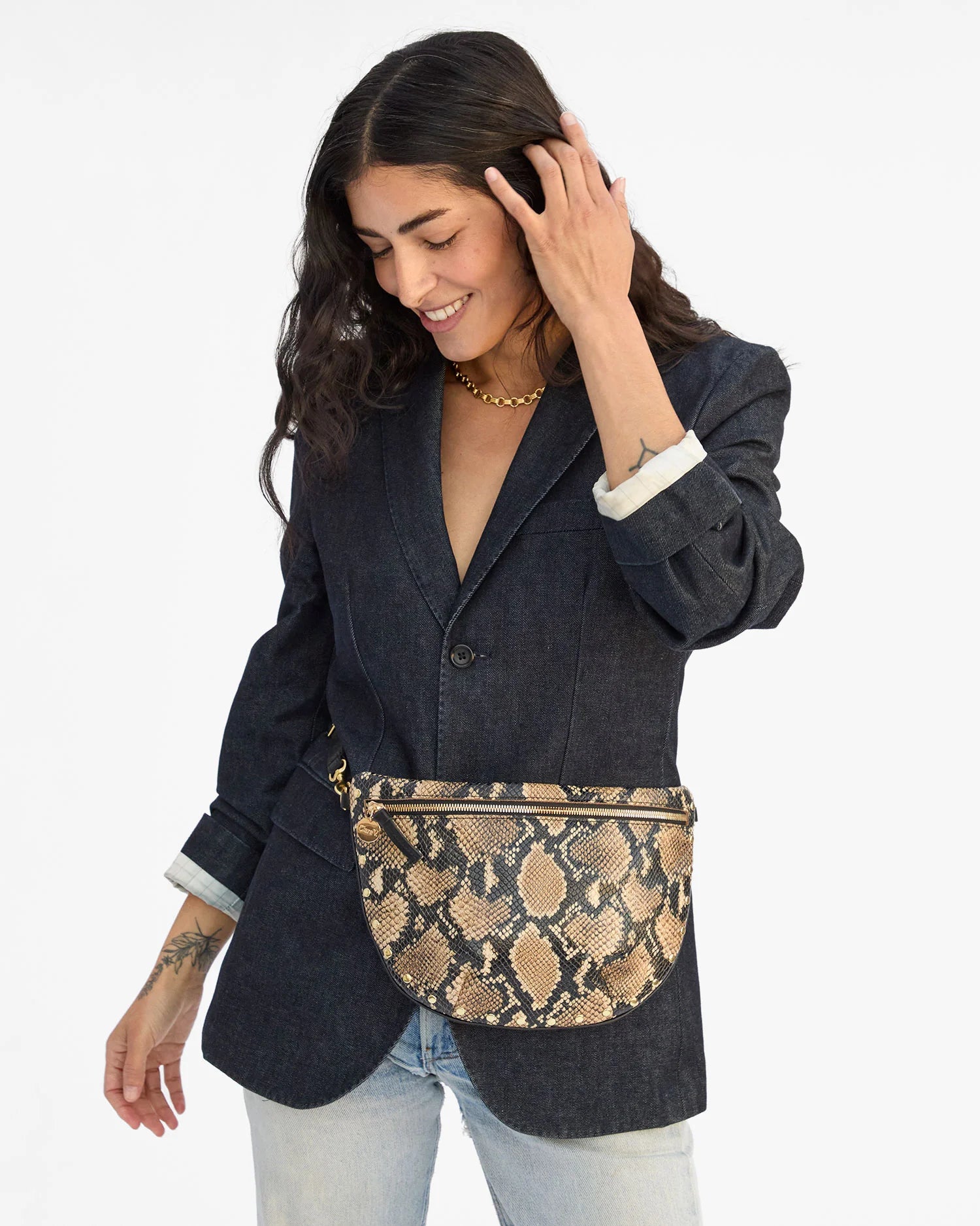 Woman wearing a dark denim jacket and snake print belt bag on a white background
