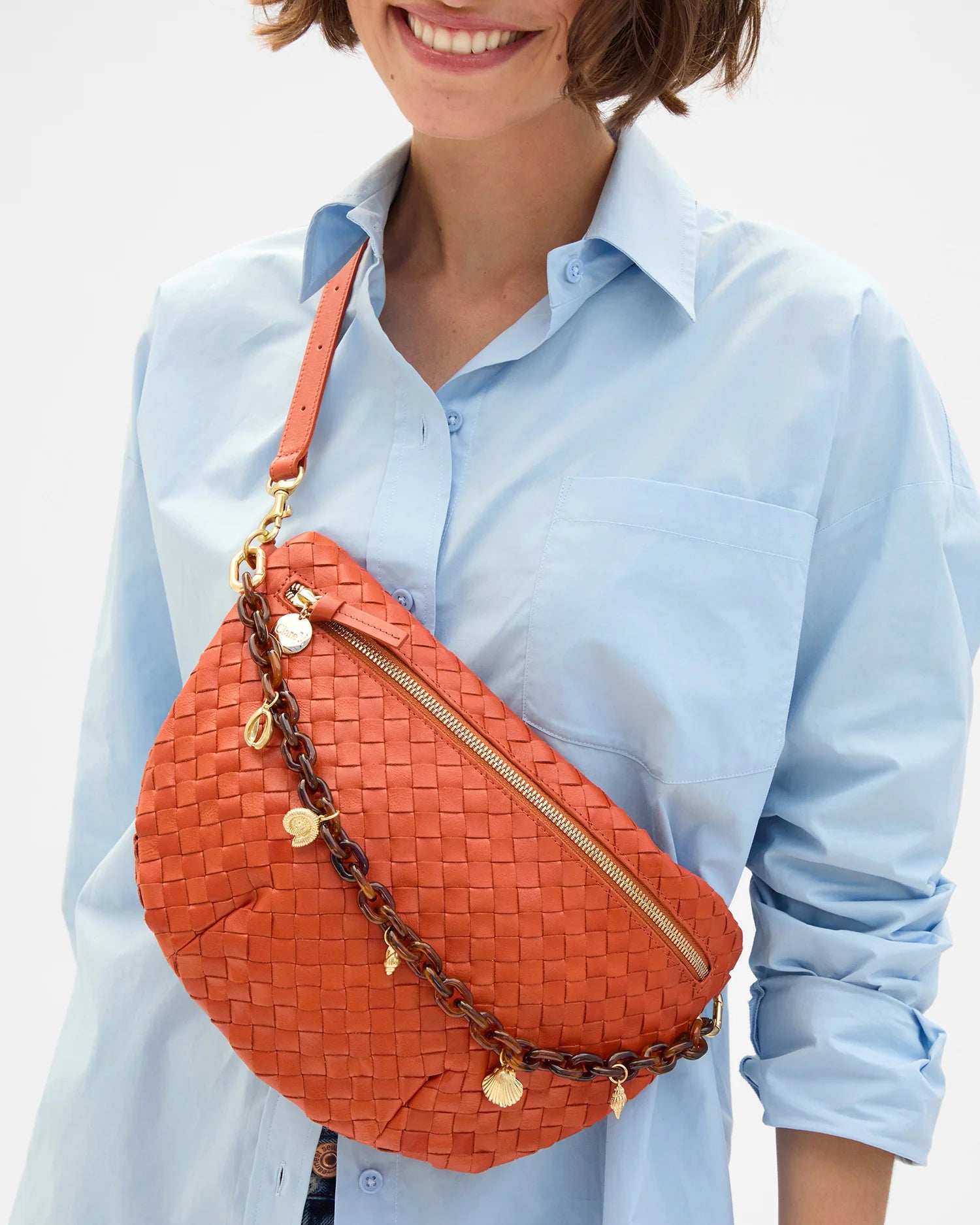 Person wearing a light blue shirt with an orange woven handbag featuring gold chains and embellishments.