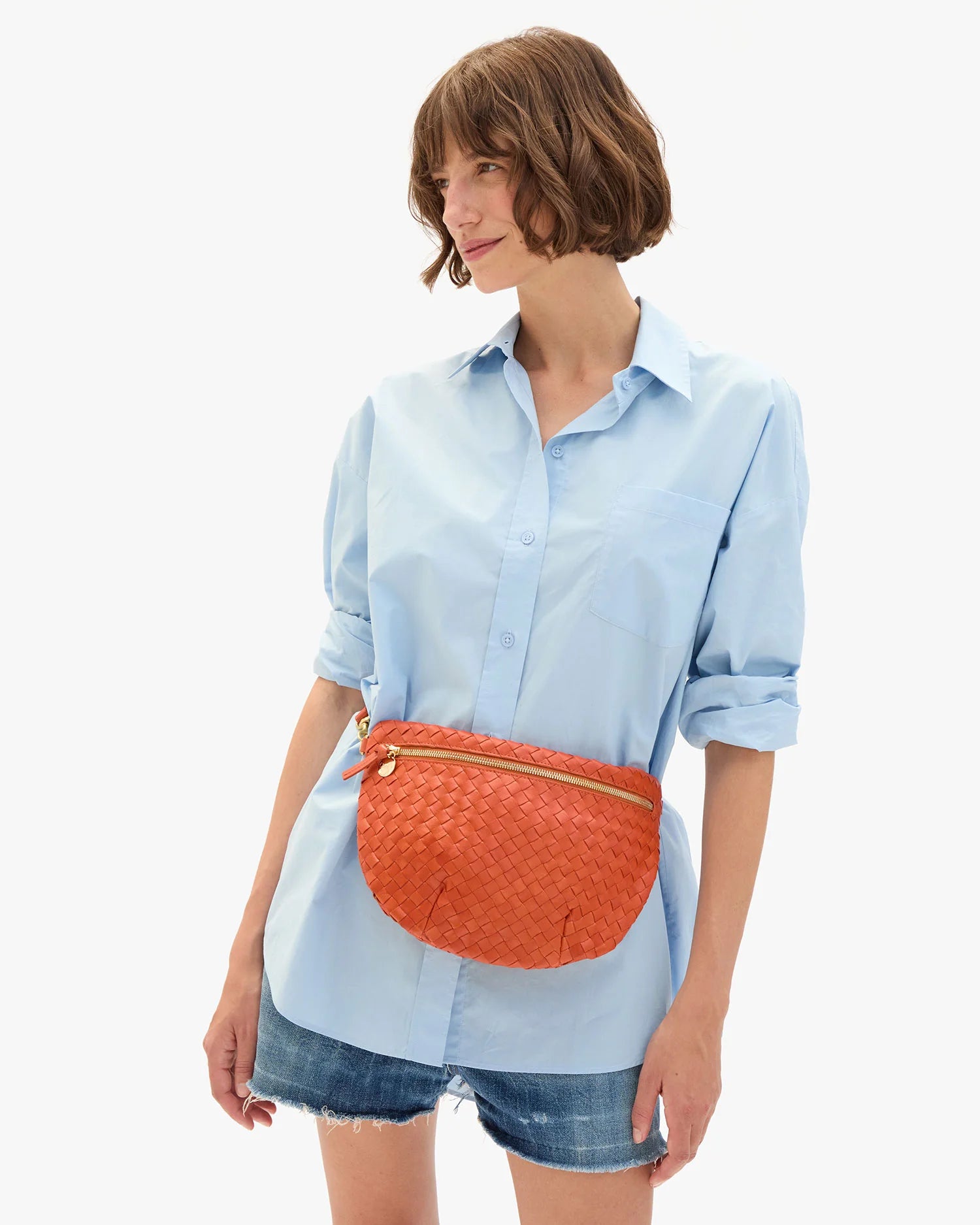 Woman wearing a light blue shirt and denim shorts with an orange waist bag on a white background