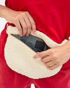 Person holding a woven handbag with a visible brand logo against a red background