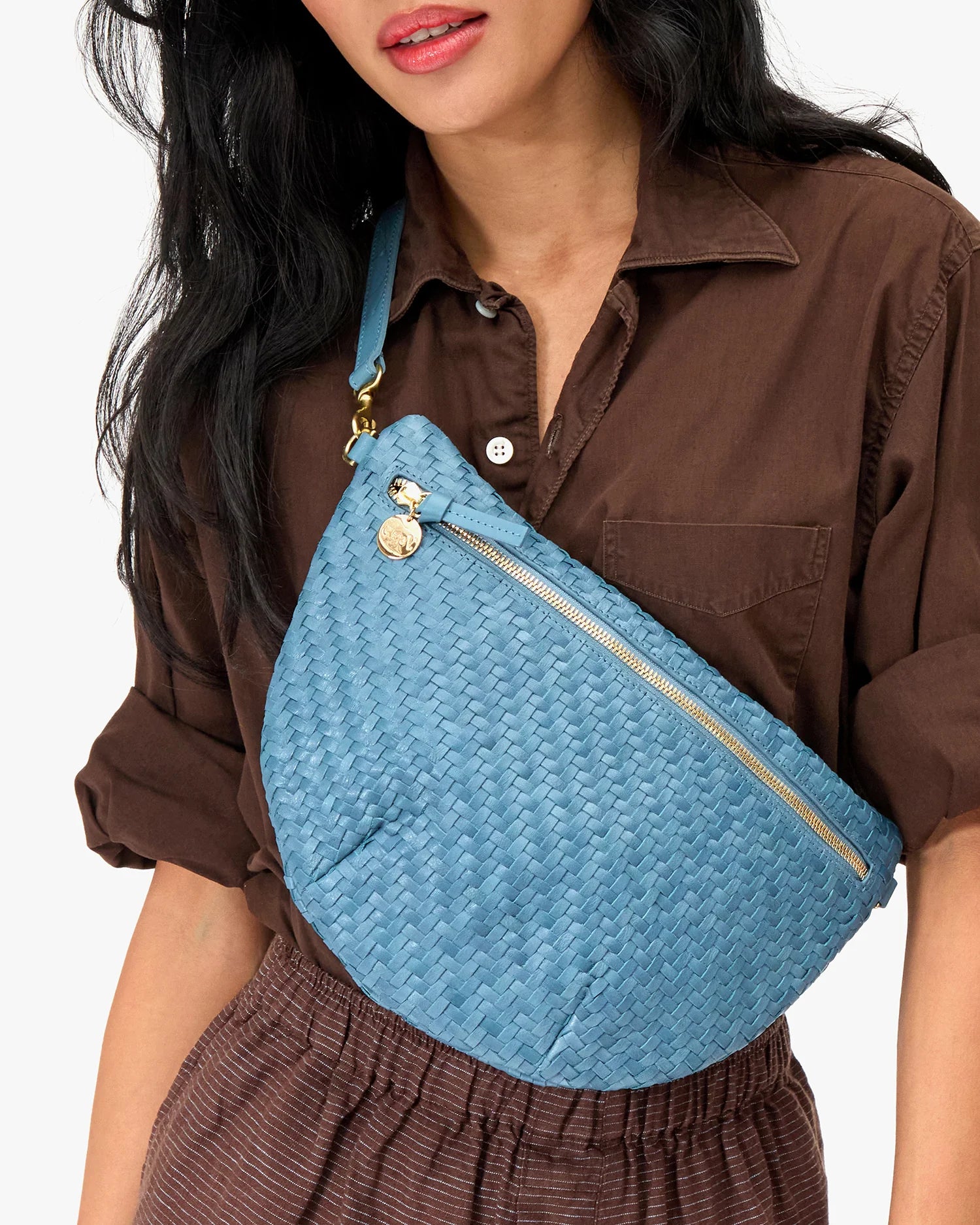 Person wearing a blue woven bag over one shoulder on a plain background