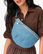 Person wearing a blue woven bag over one shoulder on a plain background