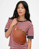 Woman wearing a striped shirt with a brown woven bag over her shoulder on a white background