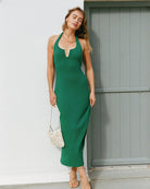 Woman in a green dress standing against a white wall with a gray door.