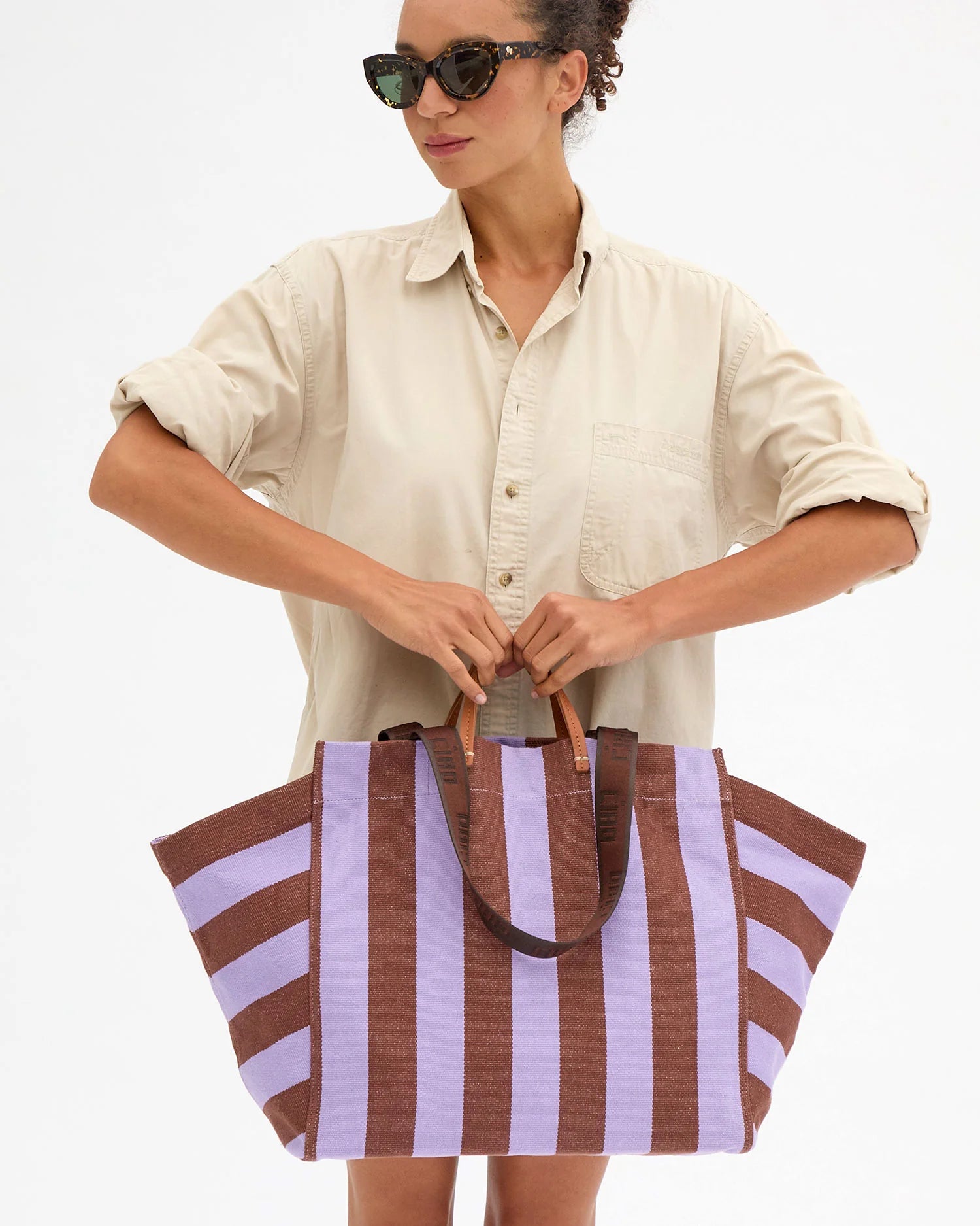 Woman holding a striped tote bag against a white background