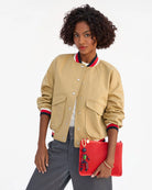 Woman wearing a beige varsity jacket with red and blue accents, holding a red clutch with a character design.