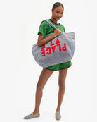Woman holding a large striped bag with 'PLAGE' text on a white background