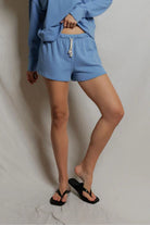Person wearing a blue outfit with shorts and a sweatshirt on a plain background