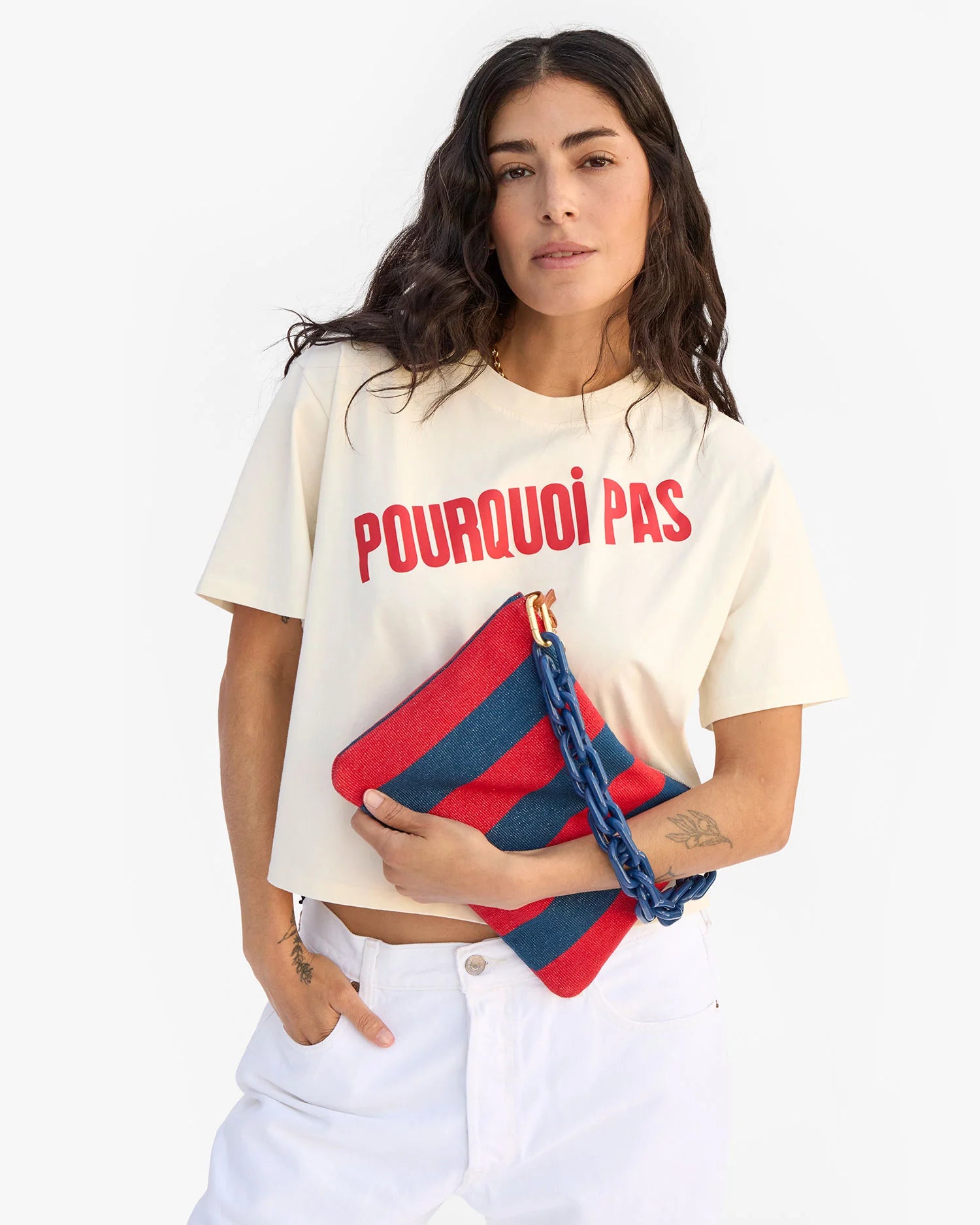 Woman wearing a white t-shirt with 'POURQUOI PAS?' text, holding a red and blue striped bag.