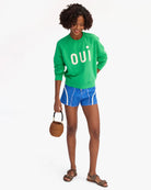 Woman wearing a green 'Oui' sweatshirt and blue shorts on a white background