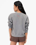 Person wearing a gray sweatshirt with a red design on the back, standing against a white background.
