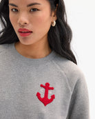Gray sweatshirt with a red anchor design worn by a person on a white background