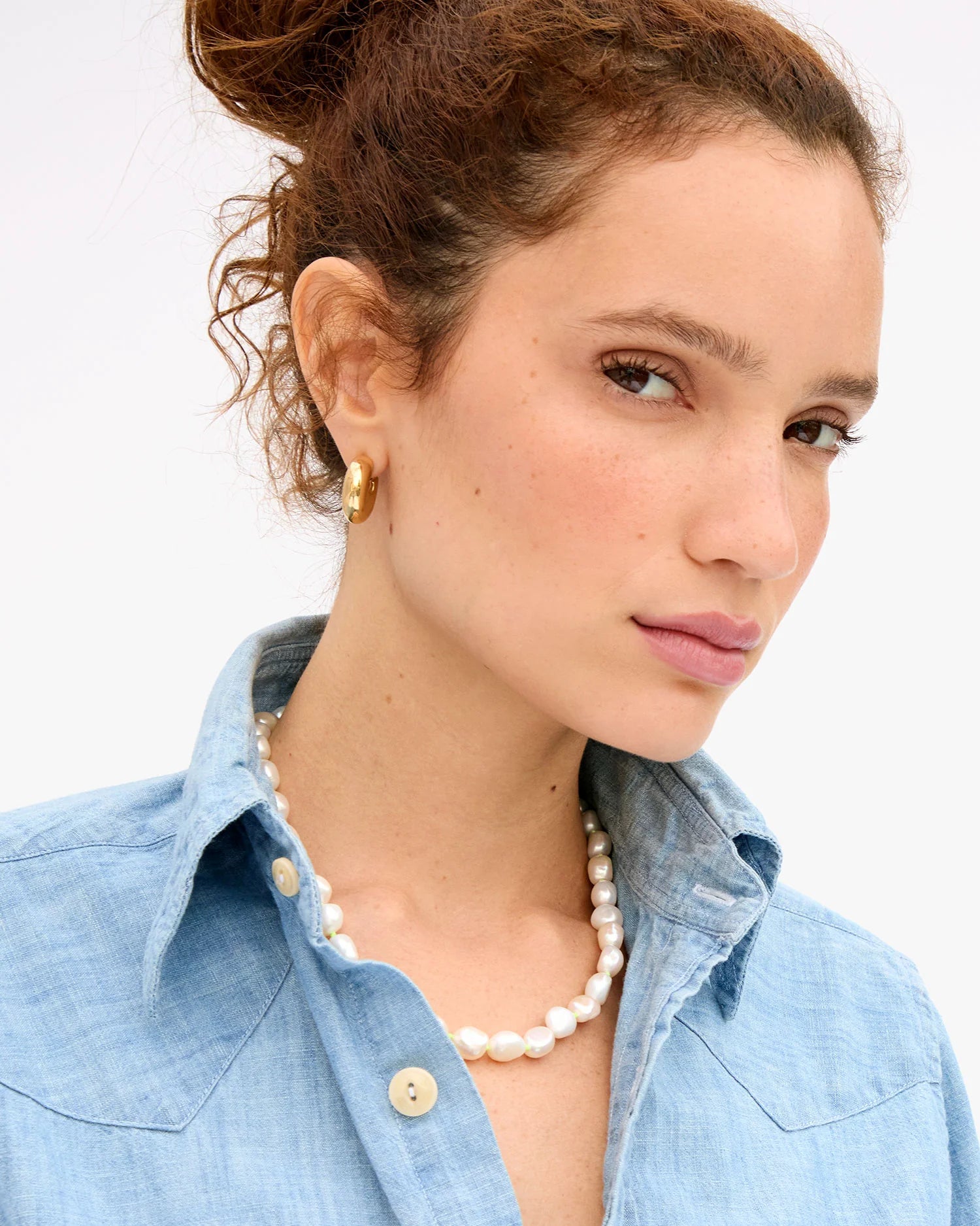 Woman wearing a pearl necklace and gold earrings with a light background