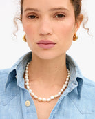 Woman wearing a pearl necklace and gold earrings with a light background