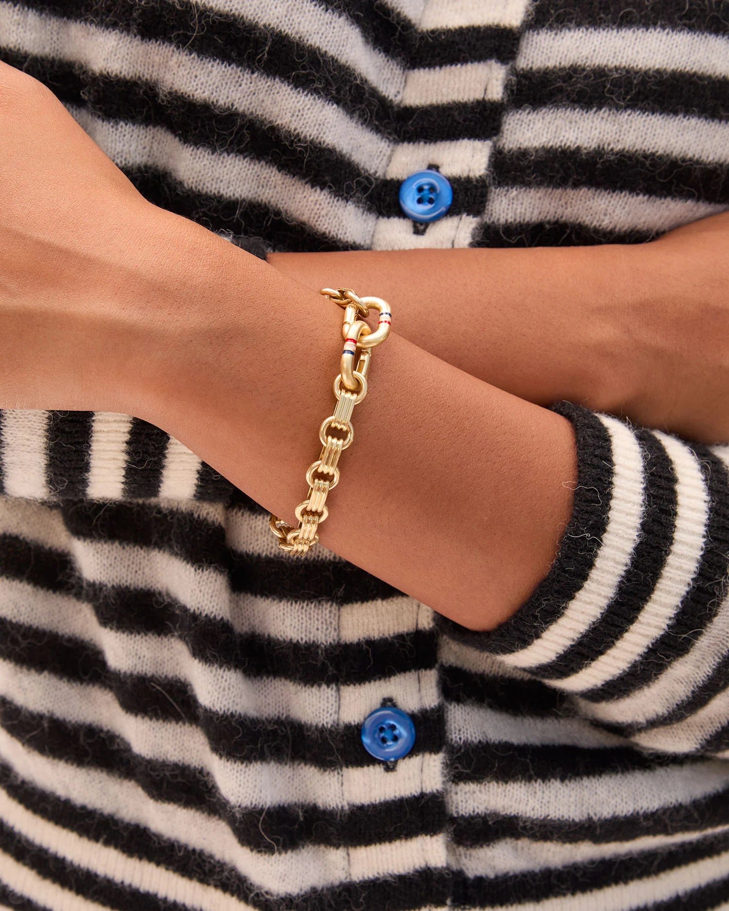 Gold chain bracelet on a wrist with a striped cardigan background